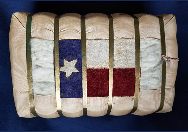 This small bale of cotton was presented to Mrs. Harrison during a Presidential visit to Galveston, Texas, April 18, 1891. It is covered on all sides with a grosgrain silk fabric, but the fabric comes around the two wide sides partially leaving a small 