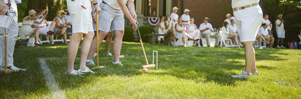Photograph of people playing croquet on the lawn of the Presidential Site, all dressed in white on a warm sunny day.