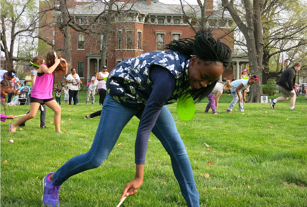 Photographic image of a girl playing egg roll on the lawn of the presidential site.