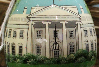 Photograph of china available in the giftshop, decoratively adorned with a panting of the white house with bushy shrubs and a pale blue sky.