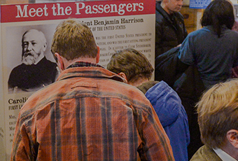 Photograph of several tourists at the benjamin harrison home, taken from behind as they peruse an exhibit titled, 
