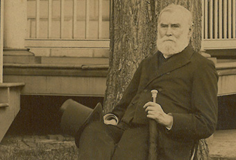 Photo of benjamin harrison, seated in front of an oak tree at mount vernon. His top hat rests on his right knee, while he holds his cane in his left hand.