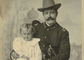 Photo of Russell Benjamin Harrison and his son. Russel is seen wearing a military uniform, with a sword at his side and a brimmed hat on his head. His son is dressed in all white.