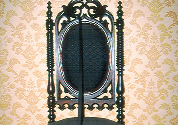 Gothic or Elizabethan rival chair circa 1850 that belonged to the Harrison family. It has been reupholstered in horse hair fabric with a diamond pattern. Back of chair is an oval shape with carved top ornament and side spooled spindles. Legs are also spooled spindles.
