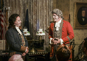 Photographic image of two actors dressed as ghosts of past presidents in front of a crowd in Benjamin Harrison's library.